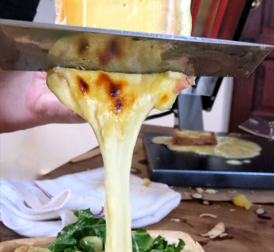 image of raclette cheese being scraped off the wheel after being melted